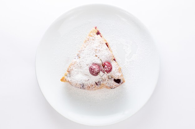 Вид сверху ломтик вишневого торта внутри белой тарелки с сахарной пудрой на белом фоне, торт, бисквит, сладкое тесто, выпечка