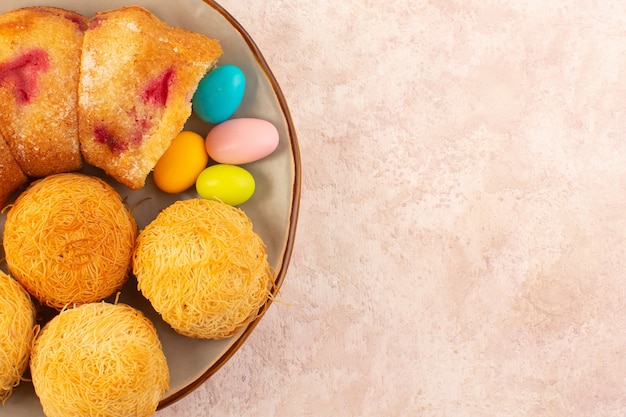 Foto gratuita una vista dall'alto fette di torta di ciliegie con caramelle e biscotti sullo zucchero rosa biscotto torta scrivania