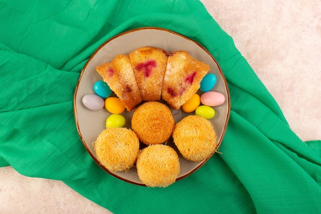 A top view cherry cake slices with candies and biscuits on the pink desk cake biscuit sweet