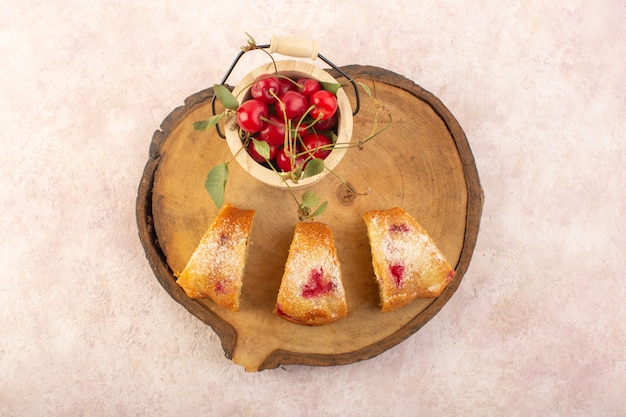 Una vista dall'alto di fette di torta di ciliegie sullo scrittorio di legno con le ciliege sullo zucchero rosa del biscotto della torta della scrivania dolce