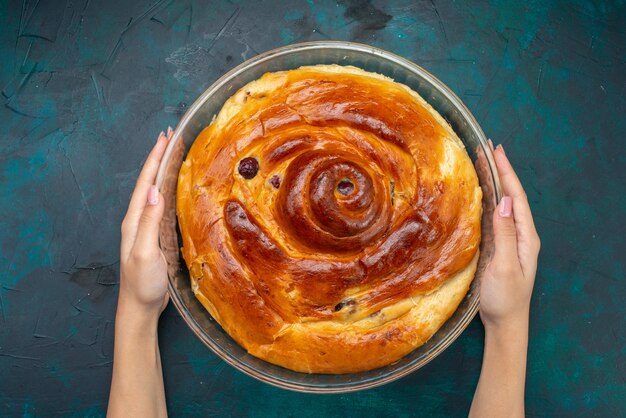 top view of cherry cake with cherries inside hold by female on dark-blue, cake sweet bake fruit darkness