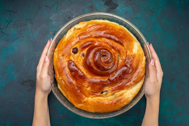 チェリーケーキの上面図は、紺色のケーキの甘い焼きフルーツの暗闇の中で女性によって保持されています