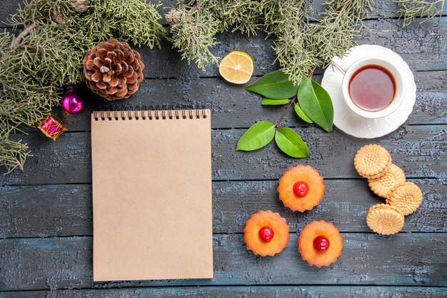 上面図桜のカップケーキモミの木の枝レモンのスライスお茶のビスケットと暗い木製のテーブルの上のノート