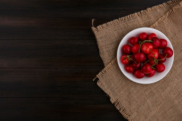 Top view of cherry on a plate on a beige napkin on a wooden surface