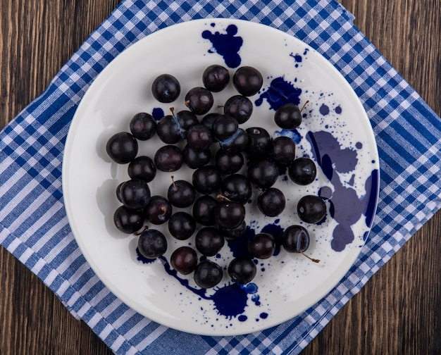 Top view cherry plum on a white plate on a blue checkered towel