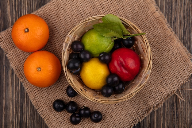 Бесплатное фото Вид сверху алычи с лимоном, лаймом и персиком в корзине с апельсинами на бежевой салфетке