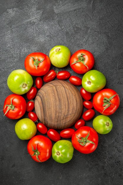 Top view cherry red and green tomatoes around a wooden plate on dark ground with free space