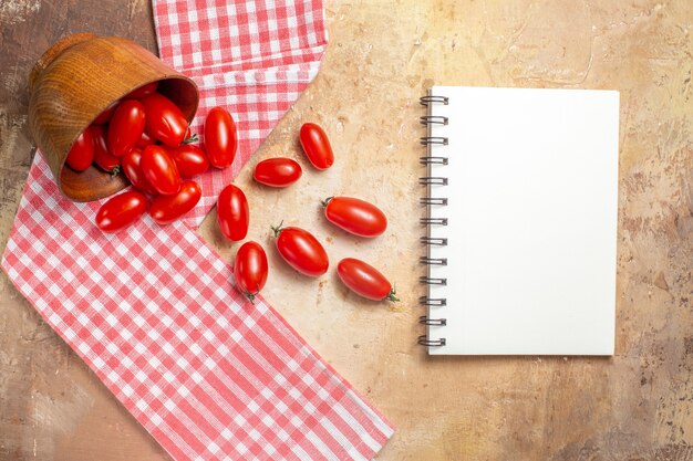 Top view cherry tomatoes scattered from bowl a kitchen towel a notebook on amber background