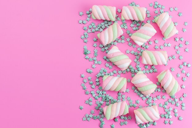 A top view chewing marshmallows colored along with star shaped green candies all on pink desk, sweet sugar candy