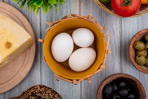 Top view chicken eggs in basket with tomato  cheese and olives on gray background