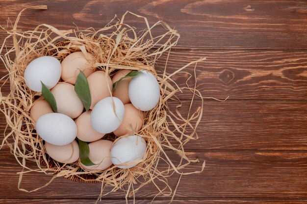 Top view of chicken eggs on nest with leaves on a wooden background with copy space