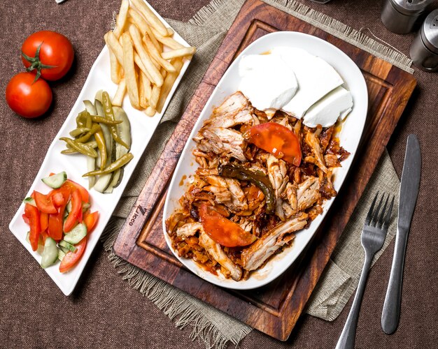 Top view of chicken kebab with tomato sauce served with yogurt fries pickles and vegetables