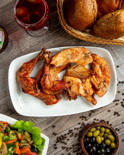 Top view of chicken legs and wings kebab arranged in a plate with a glass of wine on the wooden table