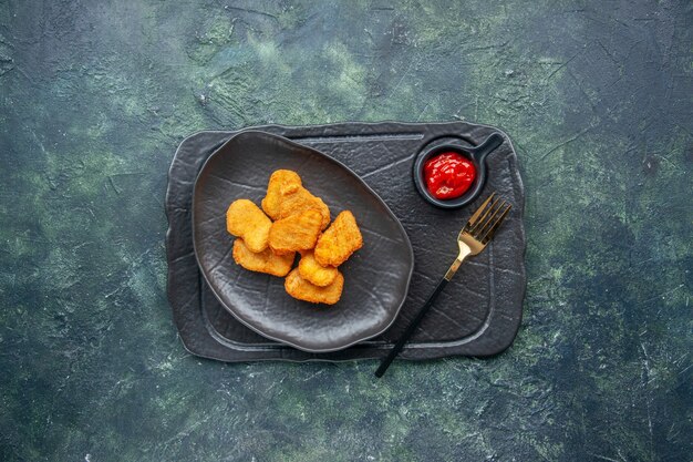 Top view of chicken nuggets on a black plate and fork ketchup on dark color tray on dark surface