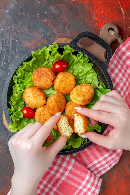 Top view chicken nuggets lettuce cherry tomatoes in pan nugget in female hands on dark surface