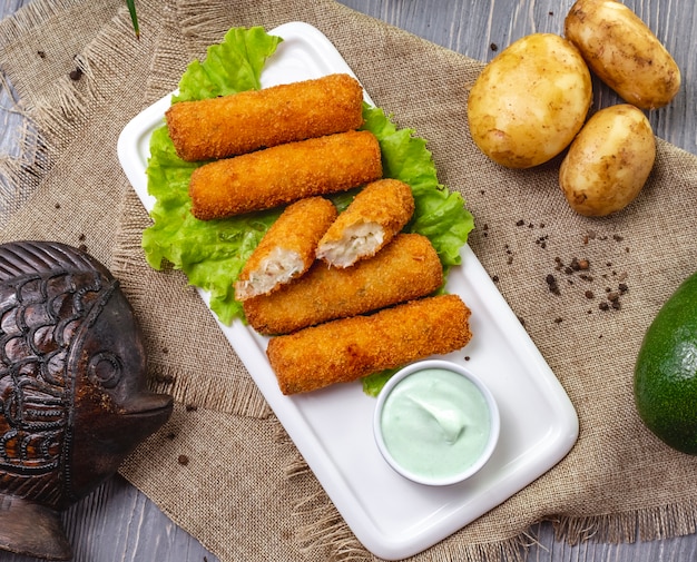 Top view chicken nuggets on lettuce with sauce and unpeeled potatoes