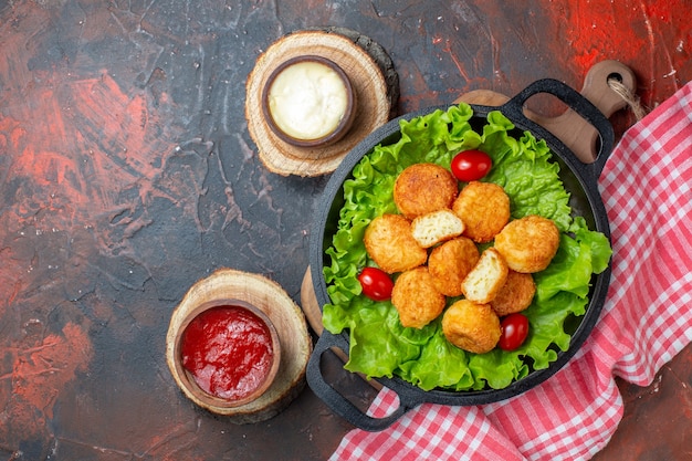 Foto gratuita pepite di pollo vista dall'alto in ciotole di salsa di padella su assi di legno su parete rosso scuro con spazio libero