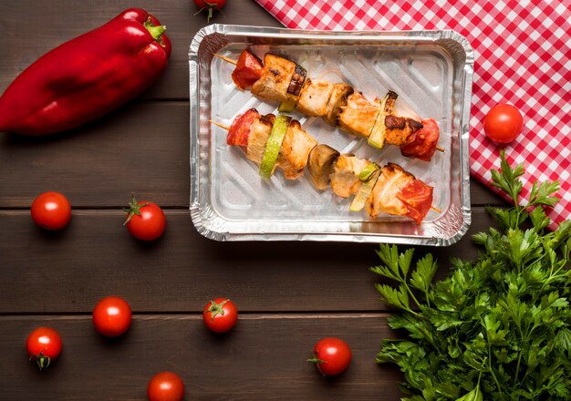 Top view chicken skewers on tray with red pepper and tomatoes