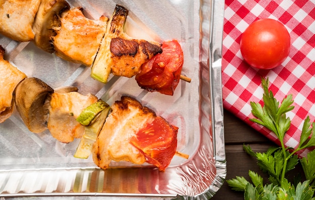 Top view chicken skewers on tray with tomato