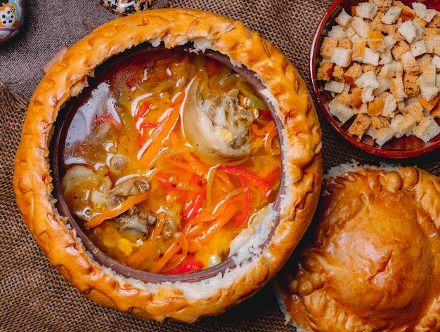 Zuppa di pollo vista dall'alto in una brocca di argilla con cracker e un coperchio di pasta