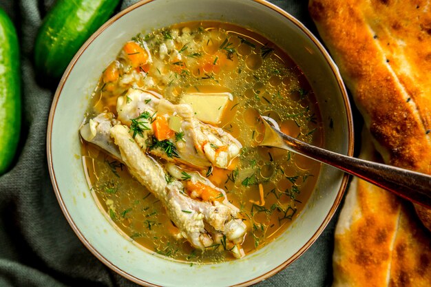 Top view chicken soup served with herbs cucumbers and bread