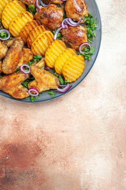 Вид сверху куриные крылышки аппетитная курица, жареный картофель, зелень и лук на тарелке