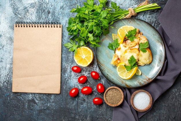 Top view chicken with cheese on plate bunch of parsley lemon cherry tomatoes notepad on grey table