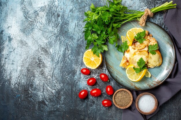 Top view chicken with cheese on plate bunch of parsley lemon cherry tomatoes spices in bowls on grey table with copy place