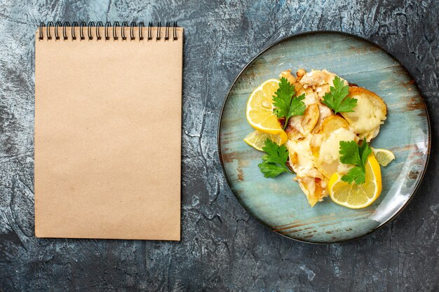 Top view chicken with cheese on plate notebook on grey table