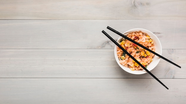 Top view of chinese fried rice bowl with black chopsticks on wooden table