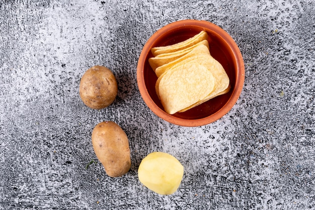 Foto gratuita chip di vista superiore in ciotola con le patate fresche sull'orizzontale di pietra bianco