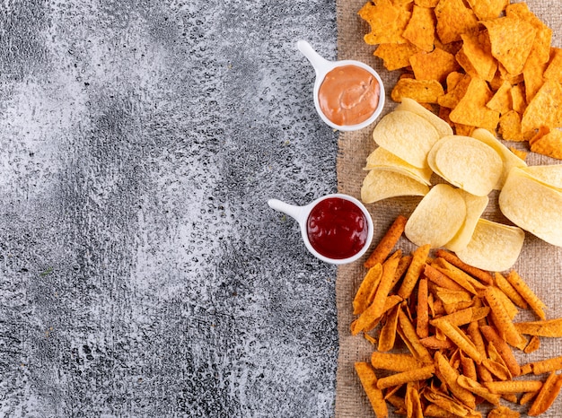 Top view chips on linen cloth with sauces in bowls with copy space on left on white stone