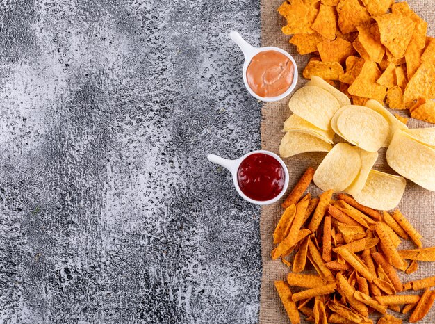 Top view chips on linen cloth with sauces in bowls with copy space on left on white stone