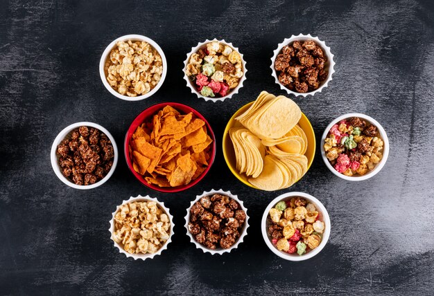 Top view of chips and popcorn in bowls on black  horizontal