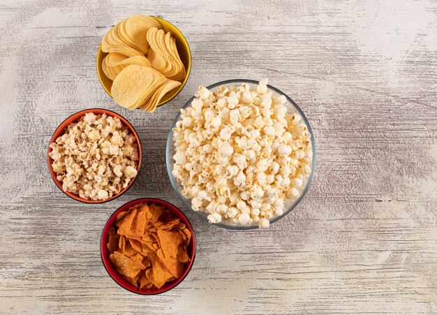 Top view of chips and popcorn in bowls on white wooden  horizontal