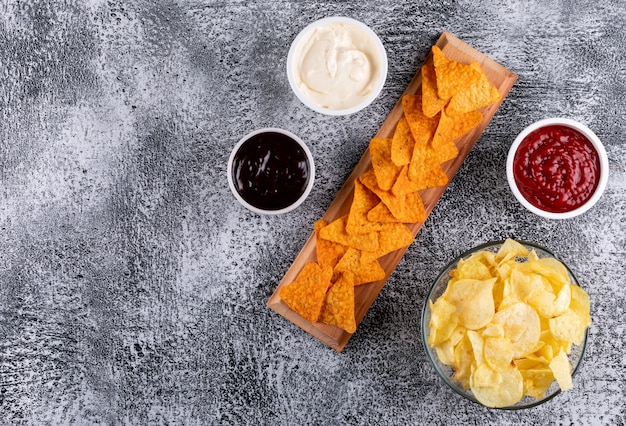 Top view chips and sauses in bowls and copy space on left on white stone