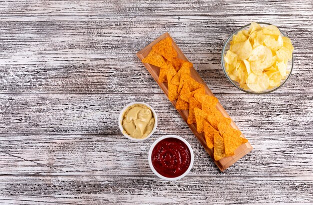 Top view chips and sauses in bowls and copy space on left on white wooden