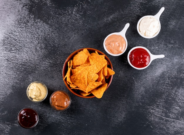 Free photo top view chips with chilli pepper and sauces in bowls and copy space on black stone