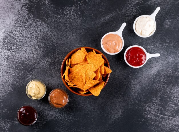 Top view chips with chilli pepper and sauces in bowls and copy space on black stone