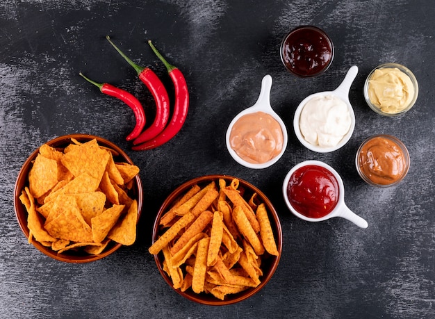 Chip di vista superiore con peperoncino e salse in ciotole sull'orizzontale di pietra nero