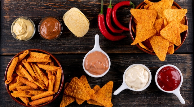 Top view chips with chilli pepper and sauses in bowls on brown wooden  horizontal