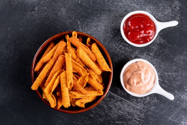 Top view chips with sauses in bowls on black stone