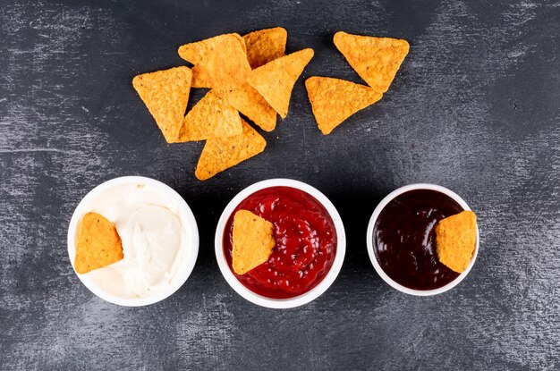 Top view chips with sauses in bowls on black stone