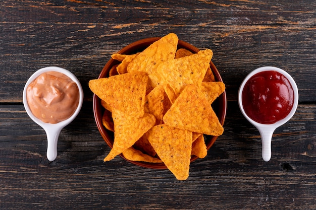 Top view chips with sauses in bowls on brown wooden