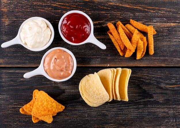 Top view chips with sauses in bowls on brown wooden