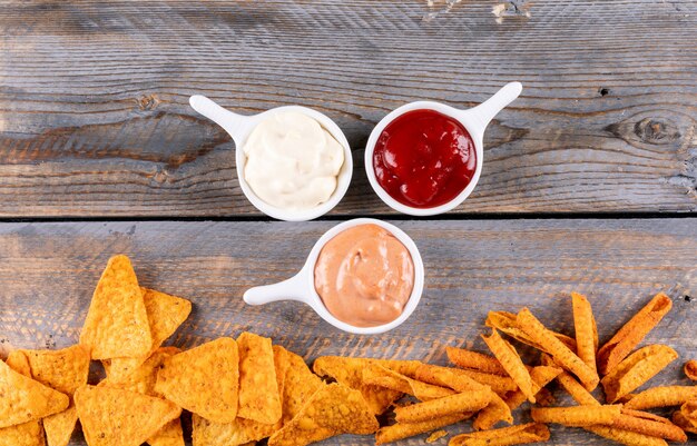 Top view chips with sauses in bowls on brown wooden