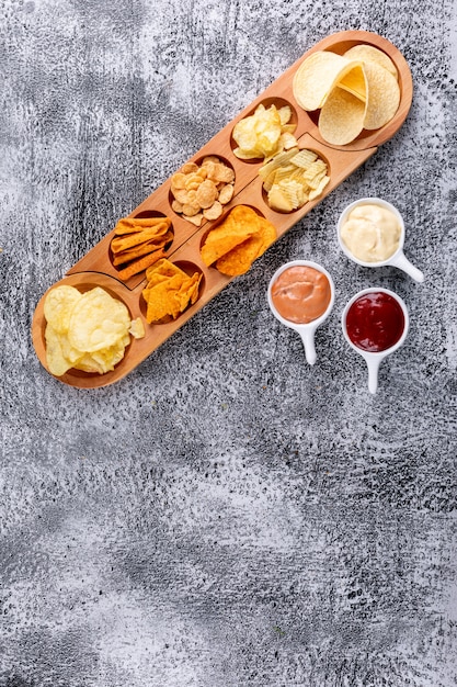 Top view chips on wooden plate with sauses and copy space on white stone  vertical