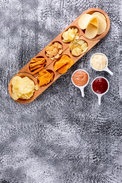 Top view chips on wooden plate with sauses and copy space on white stone  vertical