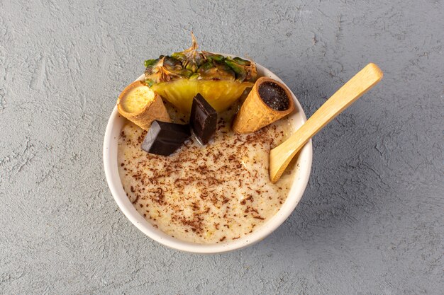 A top view choco dessert brown with pineapple slice choco bars ice cream inside white plate on the grey