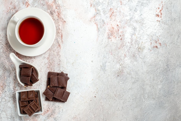 Top view of chocolate bars with cup of tea on white surface